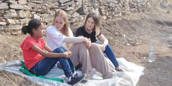 Paula Schwarz and two refugees sitting on the ground with a blanket